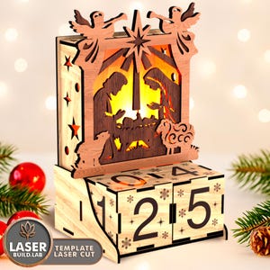 May include: A wooden Christmas advent calendar with a nativity scene cutout, angels, and a star. The calendar has a light inside, illuminating the scene. The base features rotating blocks with numbers for counting down to Christmas. The text "LASER BUILD.LAB" and "TEMPLATE LASER CUT" is visible.