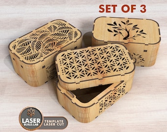 May include: Set of three wooden boxes with intricate laser cut designs. The boxes feature a geometric pattern, a leafy pattern, and a tree design. The boxes are made of light brown wood and have a natural finish.