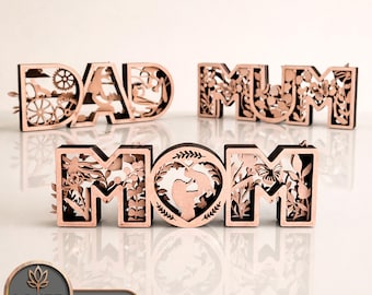 May include: Laser-cut wooden signs spelling "DAD", "MUM", and "MOM". The signs are in a light brown color with detailed floral and gear patterns. The "MOM" sign has a heart-shaped design with a mother and child silhouette.