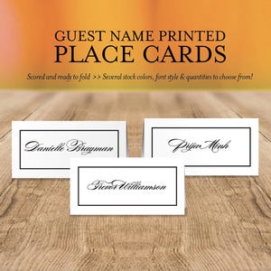 May include: White place cards with black borders and elegant script names. The cards are labeled with the names Danielle Brayman, Prija Minh, and Trevor Williamson. The text "GUEST NAME PRINTED PLACE CARDS" is at the top.