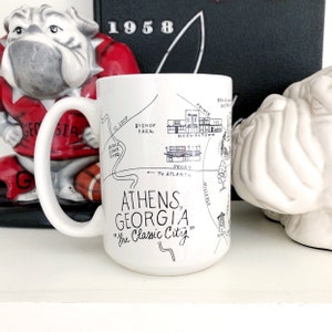 May include: White ceramic mug with a black and white illustration of a map of Athens, Georgia. The mug has the text "Athens, Georgia" and "The Classic City" printed on it.