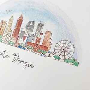 Pode incluir: Uma ilustra&ccedil;&atilde;o em aquarela do horizonte de Atlanta, Ge&oacute;rgia, com edif&iacute;cios ic&ocirc;nicos, uma roda gigante e o texto "Atlanta, Georgia".