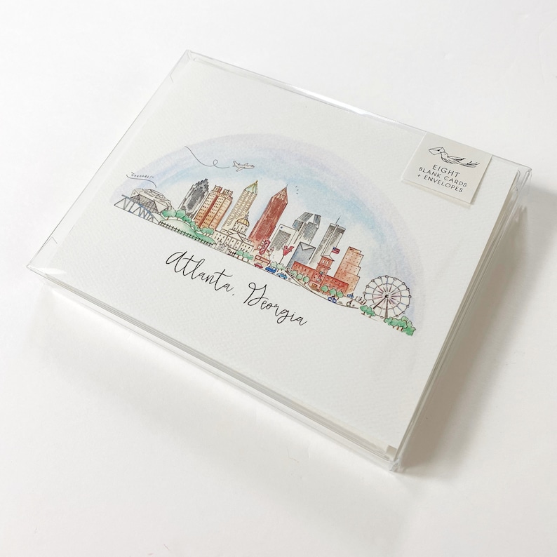 Pode incluir: Um conjunto de oito cart&otilde;es em branco e envelopes com uma ilustra&ccedil;&atilde;o em aquarela do horizonte de Atlanta, Ge&oacute;rgia. A ilustra&ccedil;&atilde;o inclui os ic&ocirc;nicos arranha-c&eacute;us da cidade, uma roda gigante e um arco-&iacute;ris.