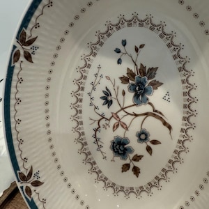 May include: White ceramic serving bowl with a blue floral design in the center. The bowl has a ribbed texture and a blue border. The floral design features blue flowers and brown branches.