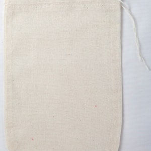 May include: A rectangular, off-white cotton drawstring bag. The bag has a simple design with a stitched top and a white drawstring. The fabric has a visible woven texture.