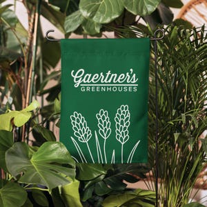 以下が含まれることがあります： 緑色のガーデンフラッグに、白い文字で「Gaertner's Greenhouses」と、白い線で描かれた3つのスタイリッシュな植物が描かれています。