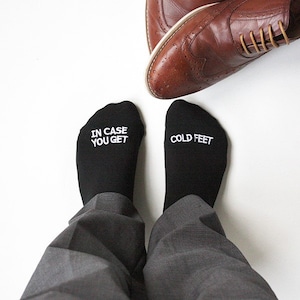 May include: A pair of black socks with white text. One sock says "In case you get cold feet" and the other says "Cold feet".