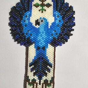May include: A beaded bracelet with a blue bird design. The bracelet is made with white, brown, blue, green, and black beads. The bracelet has gold clasps.