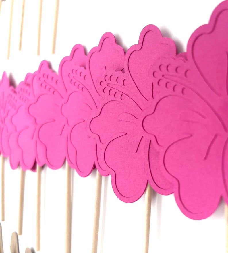 May include: Pink paper hibiscus flower cupcake toppers on wooden sticks.
