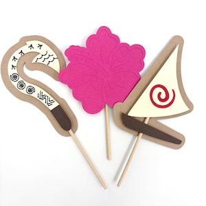 May include: Three paper cupcake toppers featuring a pink hibiscus flower, a brown and white hook, and a white sailboat with a red spiral design.