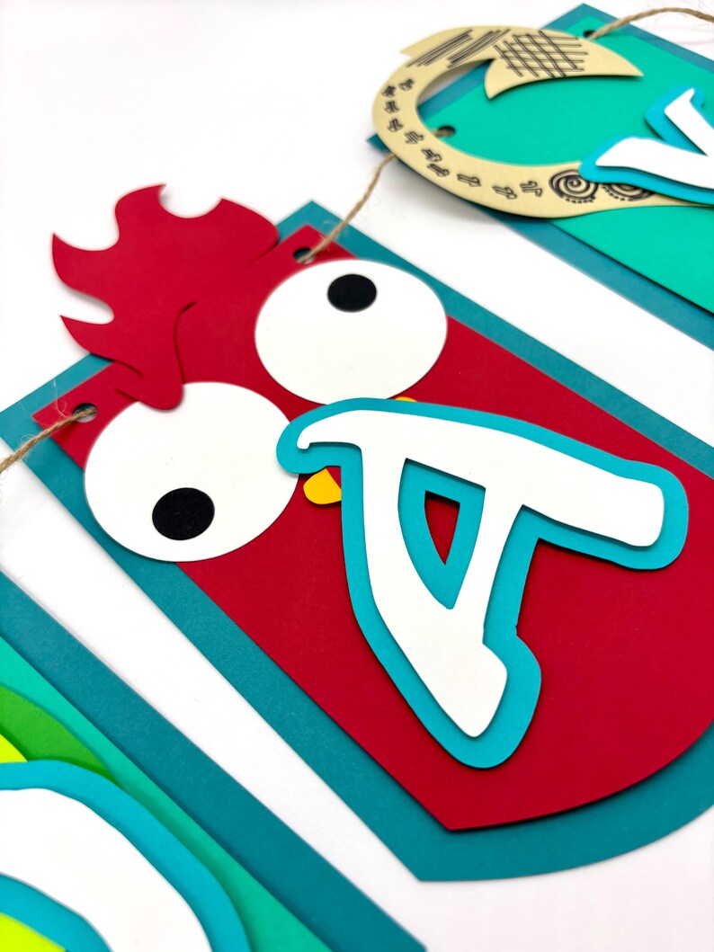 May include: A colourful paper banner with the word "Aloha" spelled out in white letters. Each letter is decorated with a different animal or design. The "A" is a red rooster with a yellow beak and large eyes. The "L" is a green palm tree. The "O" is a blue fish. The "H" is a brown horseshoe. The "A" is a green pineapple.