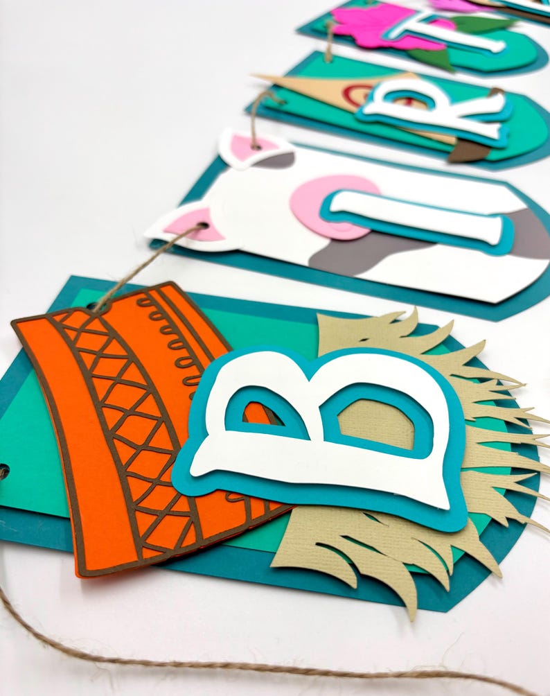 May include: A colourful paper banner with the word "Birthday" spelled out in white letters. Each letter is layered with different coloured paper and has a farm animal theme. The banner is strung together with twine.
