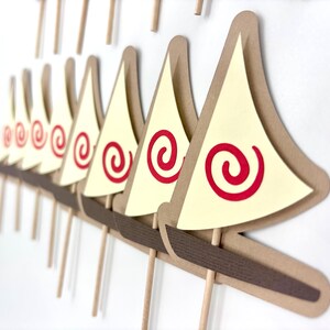 May include: A set of 10 brown paper sailboat cupcake toppers with red spiral designs on the sails. The sailboats are attached to brown sticks.