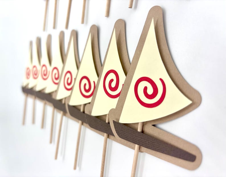 May include: A set of 10 brown paper sailboat cupcake toppers with red spiral designs on the sails. The sailboats are attached to brown sticks.