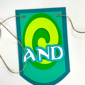 May include: A green and blue paper banner with the word "AND" in white letters. The banner has a swirl design and is strung with twine.