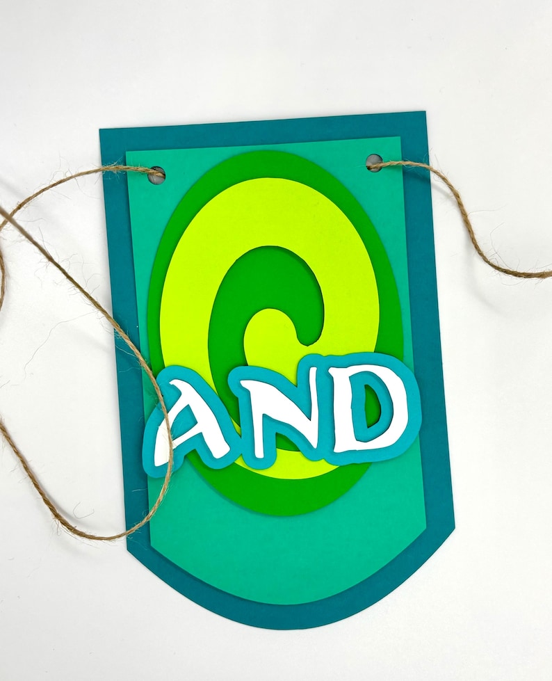 May include: A green and blue paper banner with the word "AND" in white letters. The banner has a swirl design and is strung with twine.