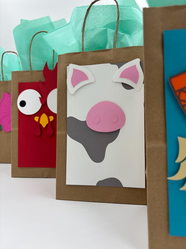 May include: Brown paper gift bags decorated with farm animal faces, including a cow, chicken, and pig. Each bag has a different animal face made of colorful paper cutouts. The bags are filled with teal tissue paper and have brown paper handles.