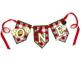 May include: A festive banner spelling "ONE" with red and white checkered pennants. Each pennant has a green border and is strung on a red ribbon. The letters are in a cream color with food-themed embellishments, including a cookie, tomatoes, and ice cream.