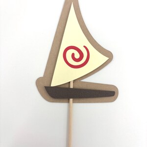 May include: A brown paper sailboat with a yellow sail and a red spiral design. The sailboat is attached to a wooden stick.