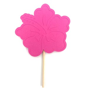 May include: A pink paper hibiscus flower on a wooden stick. The flower is a cutout shape with a detailed design.