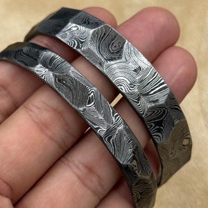 May include: Two silver bracelets with a hammered, textured finish. The bracelets are made of metal and have a unique, patterned design.