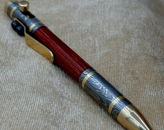 Peut inclure: Un stylo argenté et doré avec un corps en bois rouge. Le stylo possède un mécanisme de torsion et un clip.