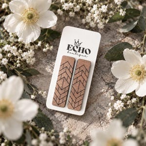 May include: A pair of rectangular wooden earrings featuring a dark brown geometric chevron and diamond pattern. The earrings are mounted on a white rectangular display card printed with the text ECHO boutique and a small crown icon above the name.
