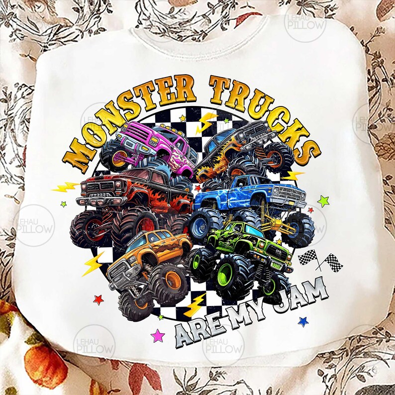 Peut inclure: Sweat-shirt blanc avec un motif color&eacute; de monster trucks. Le design pr&eacute;sente plusieurs camions violets, rouges, bleus, oranges et verts, avec le texte "MONSTER TRUCKS ARE MY JAM" dans un cercle.