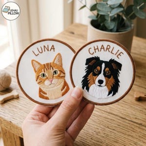Könnte beinhalten: Zwei runde bestickte Aufnäher mit braunen gestickten Rändern. Ein Aufnäher zeigt eine orangefarbene getigerte Katze mit dem darüber gestickten Namen LUNA. Der andere zeigt einen schwarz-weiß-braunen Hund mit dem Namen CHARLIE.