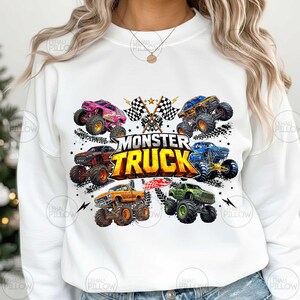 Może przedstawiać: Biała bluza z kolorową grafiką przedstawiającą sześć monster truck&oacute;w w r&oacute;żnych kolorach, w tym r&oacute;żowym, pomarańczowym i zielonym. Tekst "MONSTER TRUCK" jest widoczny nad ciężar&oacute;wkami, z szachownicami i błyskawicami.