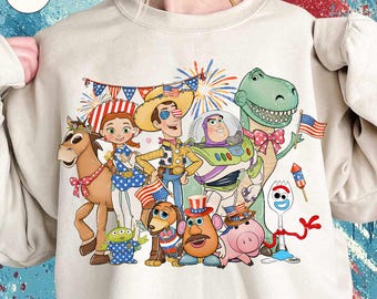 Può includere: Felpa beige con una grafica colorata dei personaggi di Toy Story che festeggiano con fuochi d'artificio e bandiere americane. I personaggi includono Woody, Buzz Lightyear e Rex, con abiti patriottici. La felpa ha girocollo e maniche lunghe.