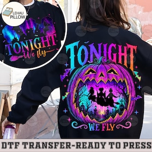 May include: A black sweatshirt featuring a large, vibrant graphic of a purple and pink jack-o'-lantern with a graveyard scene inside. The text "TONIGHT WE FLY" is printed in a colorful gradient font above and below the pumpkin illustration.