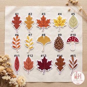 Può includere: Una collezione di quindici toppe ricamate con varie forme a tema autunnale, tra cui foglie di quercia, foglie d'acero, una pigna e un fungo. Ogni toppa è numerata da 1 a 15 e presenta colori distinti come rosso, arancione, giallo, marrone e verde.