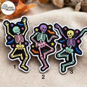 May include: Three embroidered patches featuring dancing skeletons on a black background. Each skeleton is a different colour, including mint green, purple, and yellow, with pink, mint, and purple ribcages. Small stars and bats surround the skeletons.