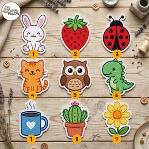 May include: A collection of nine embroidered patches featuring a white rabbit, red strawberry, red ladybug, orange tabby cat, brown owl, green dinosaur, blue coffee mug with a white heart, green cactus in a pot, and a yellow flower.