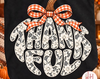 Puede incluir: Un bolso tote negro con un gráfico de calabaza grande. La calabaza está rellena con un patrón de encaje floral blanco y la palabra THANKFUL en letras negritas. Un lazo de cuadros naranja y blanco corona el tallo.