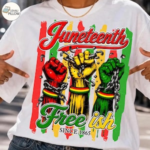 May include: White t-shirt with a graphic design celebrating Juneteenth. The design features three fists in red, yellow, and green, each with a chain, and the words "Juneteenth" and "Free ish since 1865."