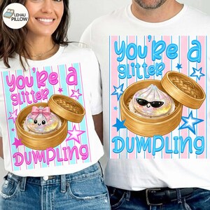 May include: White t-shirts with a colorful graphic design. The design features a cartoon dumpling in a bamboo steamer, with the text "You're a Glitter Dumpling" in pink and blue. Stars and stripes complete the design.