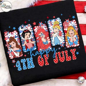 Könnte beinhalten: Schwarzes T-Shirt mit einem Design, das fünf Disney-Prinzessinnen in patriotischer Kleidung zeigt. Das Design umfasst rote, weiße und blaue Sterne und Feuerwerk, mit dem Text "Happy 4th of July" in einer festlichen Schriftart.