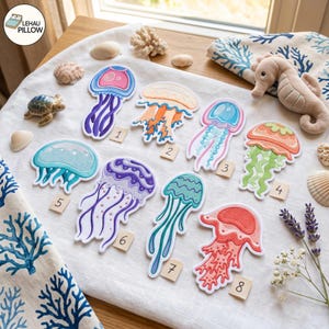 May include: Eight embroidered jellyfish patches arranged on a white fabric surface, each numbered one through eight. The patches feature various colors including pink, orange, blue, purple, teal, and red, with detailed tentacles and bell designs.