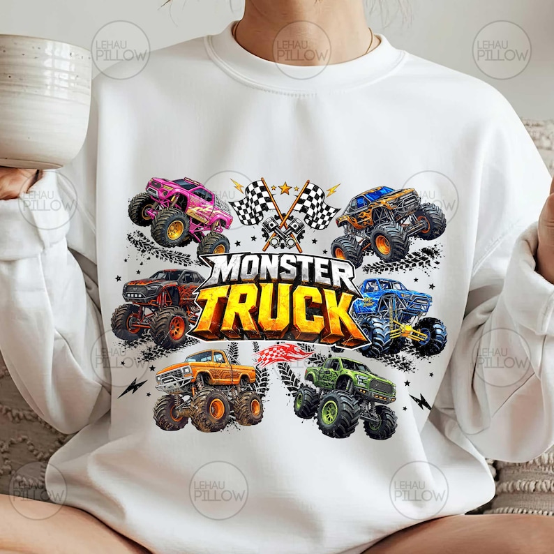 Może przedstawiać: Biała bluza z kolorową grafiką przedstawiającą kilka monster truck&oacute;w w r&oacute;żnych kolorach, w tym r&oacute;żowym, pomarańczowym i zielonym. Tekst "MONSTER TRUCK" jest wyraźnie widoczny. Wz&oacute;r zawiera r&oacute;wnież szachownice i gwiazdy.