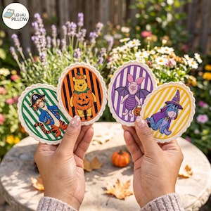 May include: Four oval-shaped fabric patches featuring Winnie the Pooh characters in Halloween costumes. Tigger wears a pirate outfit, Pooh is inside a pumpkin, Piglet is dressed as a bat, and Eeyore wears a wizard hat and cape. Each patch has a scalloped edge.