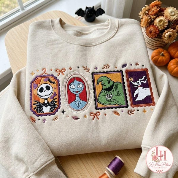 Könnte beinhalten: Ein cremefarbenes Sweatshirt mit Rundhalsausschnitt und vier rechteckigen Stickaufnähern, die Charaktere aus Nightmare Before Christmas zeigen, darunter Jack Skellington, Sally, Oogie Boogie und Zero, umgeben von kleinen gestickten Schleifen und Blättern.