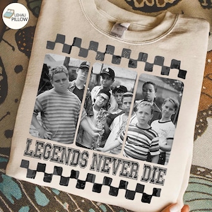 Puede incluir: Sudadera beige con una imagen en blanco y negro de un grupo de chicos. La imagen está enmarcada con un patrón de cuadros blancos y negros. El texto "LEGENDS NEVER DIE" está impreso debajo.