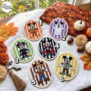 May include: Six oval embroidered patches featuring Disney characters in Halloween costumes. Patch 1 shows Mickey in a pumpkin, 2 a ghost, 3 Minnie as a witch, 4 Mickey as a vampire, 5 Mickey as a scarecrow, and 6 a zombie. Each patch has a striped background.