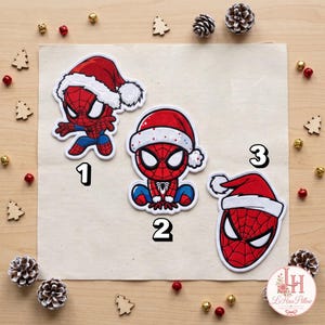 Peut inclure: Trois écussons brodés représentant un personnage de super-héros rouge et bleu portant un bonnet de Père Noël rouge à bordure blanche. Le premier écusson montre le personnage en pose dynamique, le deuxième assis et le troisième son masque.