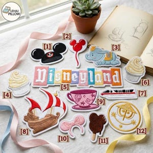 Könnte beinhalten: Eine Sammlung von zwölf bestickten Aufnähern mit verschiedenen Motiven, darunter eine schwarze Mausohren-Mütze, ein roter Ballon, ein blauer Elefant, ein buntes Disneyland-Schild, Cupcakes, ein Schiff, eine rosa Teetasse, eine Einschienenbahn, rosa Ohren, eine Schokoladenleckerei und eine goldene Sonne.