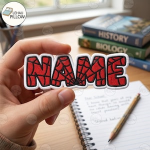 May include: A custom embroidered patch featuring the word NAME in bold, red block letters with a black spiderweb pattern. The letters are outlined in thick white thread, creating a cohesive, durable design suitable for attachment to fabric items.