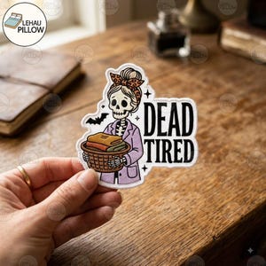 Op de afbeelding: Een gestanste sticker met een skelet dat een hoofdband met luipaardprint en een lichtpaarse blazer draagt, terwijl het een bruine wasmand met opgevouwen kleding vasthoudt. De tekst DEAD TIRED staat in het zwart ernaast met een kleine vleermuis.