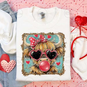 Peut inclure: Sweat-shirt blanc avec une vache des Highlands de dessin anim&eacute; portant des lunettes de soleil en forme de c&oelig;ur et une bulle de chewing-gum. La vache a un n&oelig;ud rouge et est entour&eacute;e de c&oelig;urs. Le motif est encadr&eacute; d'une bordure l&eacute;opard.